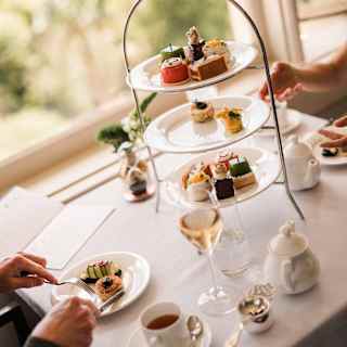 Angled image of guests enjoying sweet and savoury bites from a three-tier stand with wine at a Botanica Afternoon Tea.