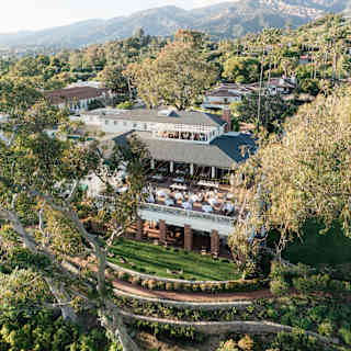 Aerial view of El Encanto's stack of terraces, lawn and gardens, surrounded by eucalypts, with rugged mountainous backdrop.