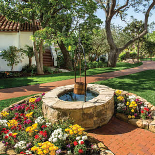 An ornamental well surrounded by colourful flowerbeds among rooms and trees in the seven-acre hotel gardens
