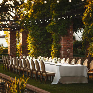 Low sunlight catches an elegant table laid for 24 diners alongside a pretty lily pond in the hotel’s arbor gardens