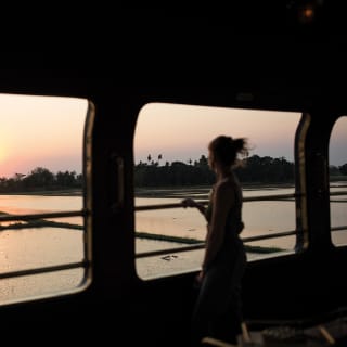 Lady gazing across the Thai countryside from an open-air train observation car