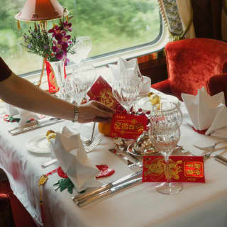 A waiter places red and gold lucky money bags on a table in Malaya Dining Car, decorated and laid for a celebration meal.