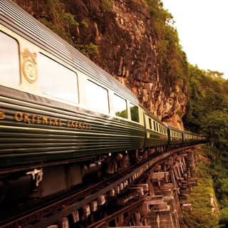 Vagões de trem verde e creme passando por uma ponte ferroviária de madeira