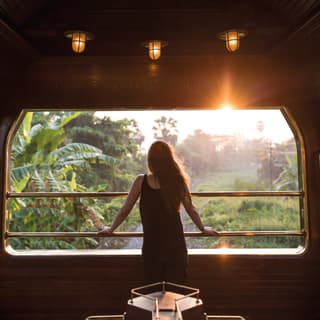 Lady looking out of an open-air train observation carriage at the sunrise beyond