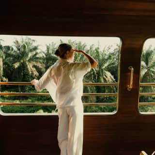 A woman in translucent white top and trousers shields her eyes as she gazes at the view from the Observation Deck rails.