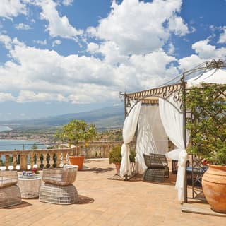 Lemon trees in terracotta pots dot a vast terrace, furnished with an elegant wrought iron gazebo and rattan easy chairs