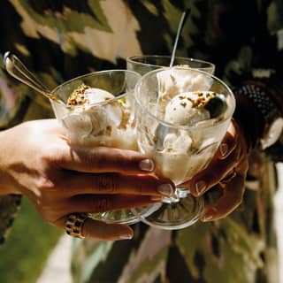 Close-up of a lady's hands clasping three glasses filled with gelato and topped with chopped nuts