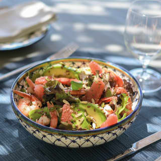 A fresh salad of leaves and avocado, pink grapefruit and king prawns, sprinkled with seeds is served in a majolica bowl