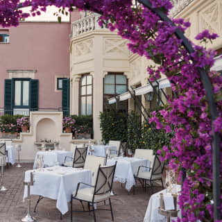 Purple flower arch leading to a restaurant balcony with linen-coated tables