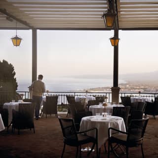 A waiter finishes laying tables for dinner service as the light lowers over the restaurant terrace with stunning views of the bay