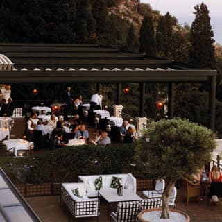 Diners sit to eat al fresco as dusk settles over the terrace restaurant, surrounded by olive trees and lit by lanterns