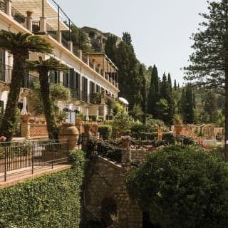 The Hotel's white stone facade climbs up the mountain side, in a lush garden of date palms, stone pines and Italian Cypresses