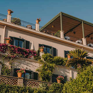 Low-angle view of a shaded rooftop dining terrace, which sits above hotel rooms with doors opening onto balconies in bloom.