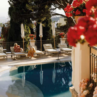 Guests reclining on sunbeds by a calm outdoor pool surrounded by Mediterranean gardens