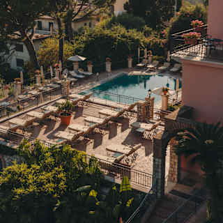 Three rows of loungers face the light on a sun terrace adjacent to the hotel pool, overlooking gardens, viewed from above.