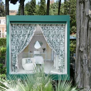 Open green floral curtains reveal the stylish interior of a Dior Garden of Dreams treehouse-style treatment pod