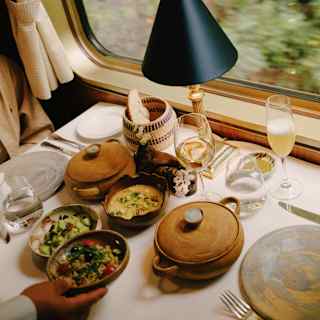 A waiter places a dish of grain salad on a table already busy with lidded pots and lunch bowls containing vibrant vegetables.