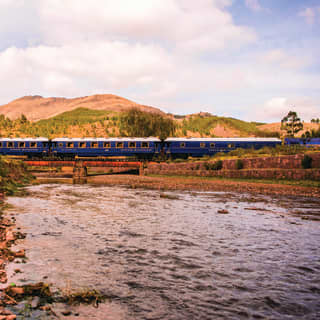 Royal blue train carriages stretching across a bridge over a rocky river
