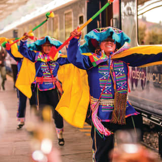 Man in colourful traditional Peruvian dress dancing alongside a train