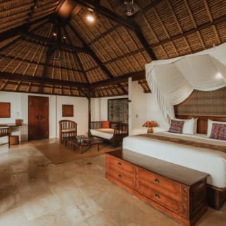 View across the Cottage Suite, with a large bed and canopy, simple furniture and abundant space under a high alang-alang roof.