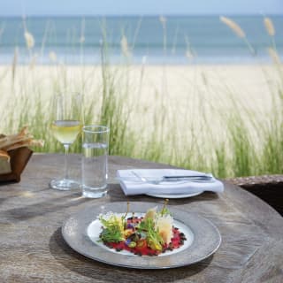 Close-up of a salad dish on a table beside a sandy beach
