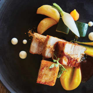 An elegantly dressed black plate of pork belly confit in Balinese spice with saffron apple puree, from Nelayan restaurant.