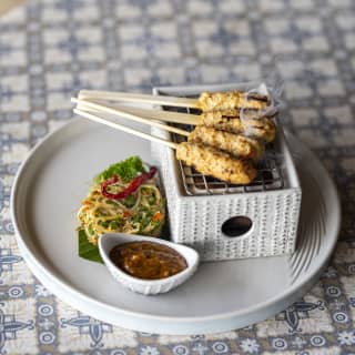 Four sticks of Bali speciality, Satay Lilit, rest on a miniature ceramic grill with steamed vegetables and a peanut sauce.
