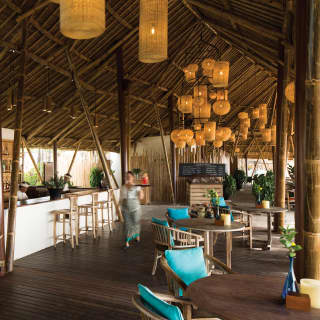 Inside Nelayan, wicker lights hang from a high ceiling supported by thick bamboo poles above wood and sapphire furnishings.
