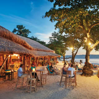 Open-air thatched beach hut bar on a white sandy Balinese beach at sunset