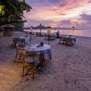 In lilac evening light, the beach is dotted with tables and lamps, offering Nelayan's guests a waterside dining experience.
