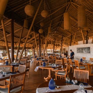View over Nelayan's terrace where multiple ceiling beams echo the slatted wood dining chairs and plentiful bamboo supports.