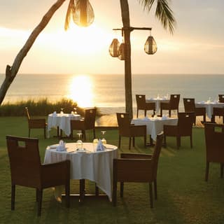 View of formal dining tables on a restaurant lawn terrace at sunset over the beach