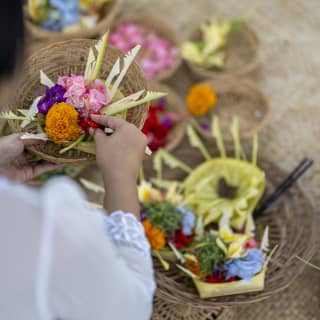 Looking down on a woman creating Hindu offerings, called Canang Sari, with bright, exotic blooms placed on wicker trays.