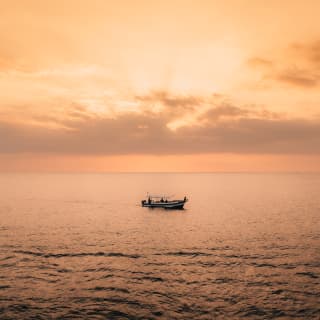 The Dedari boat sails across the silvery sea in a wide shot, taken at sunset with a soft peach sky and thin grey clouds.