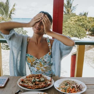 Mujer cubriendo sus ojos con sus manos alegremente en una mesa llena de platos de mariscos
