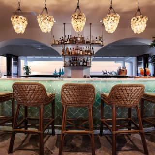 Five rattan bar stools in front of a turquoise tiled bar counter