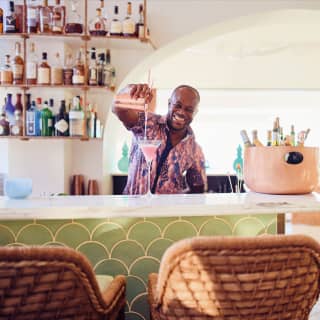 Smiling barman pouring a pink cocktail on a marble bar counter