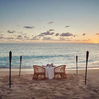 Private beach table at sunset with fire-lit torches framing a sea view