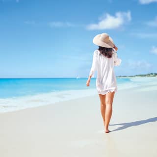Woman walking along Baie Longue shore under sunny blue skies