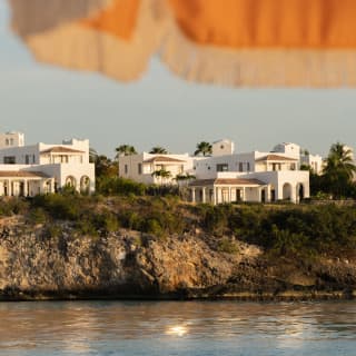 White villas line the clifftops at the south end of Long Beach, seen from beneath the fringe of an orange and white parasol.
