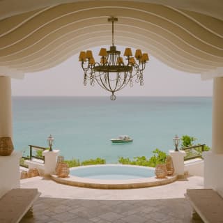 View from the cool stone lobby with undulating ceiling, chandelier and pool, out to sea where a boat floats in the blue.