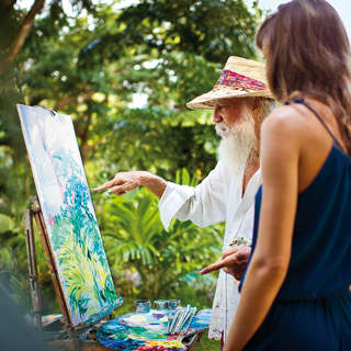 Woman in navy dress and Sir Roland Richardson painting on a canvas in tropical gardens