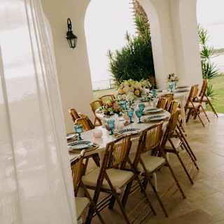 Angled view of a curvy, elegant celebration table on a pool villa terrace, taken from a doorway, part-obscured by a drape.