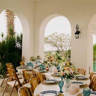 A villa terrace transforms into a celebration venue with a curved white table lined with blue glasses, plates and flowers.