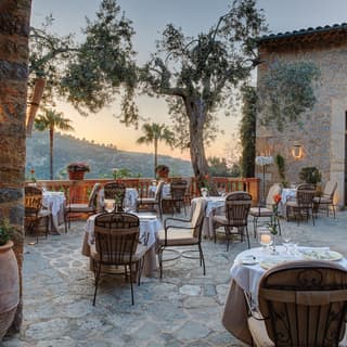 Stone-tiled restaurant patio dotted with formal candlelit tables at sunset