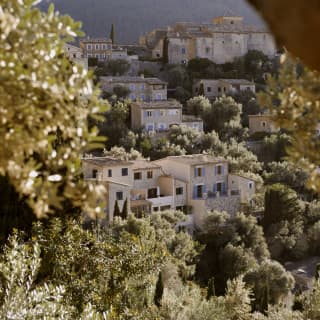Looking from the sunny hotel grounds through the overhang of an olive tree towards Deià's hillside homes in soft shade.