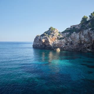 The still sea is a palette of aquamarine, turquoise and cobalt in the small cove at Cala Deia, surrounded by limestone cliffs