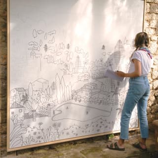 An artist works on a giant drawing of Deia, including La Residencia, its gardens, pool and the town itself as it climbs the hills