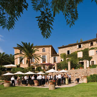Guests at a garden party among lush gardens outside a stone-built Spanish villa