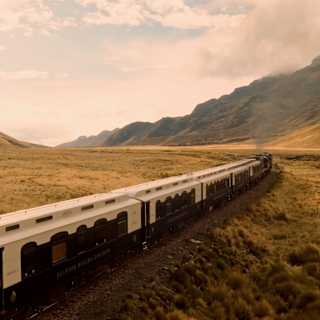 The Andean Explorer lets off steam as it heads through an Altiplano valley, with mountains either side, seen from just above.